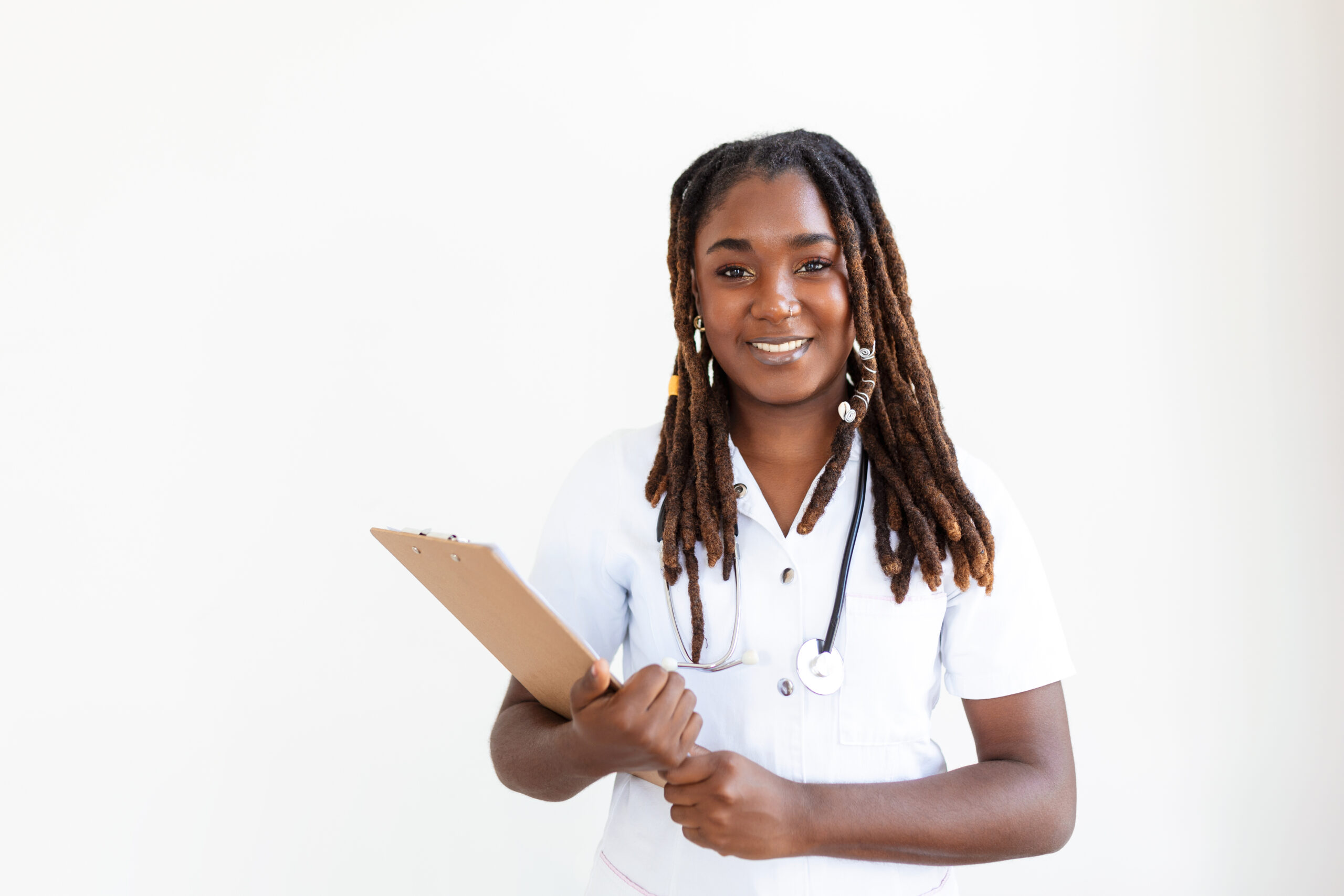 emale nurse or doctor smiles while staring out window in hospital hallway and holding clipboard with patient file. African American female pediatric nurse in office. Portrait Of Female Nurse Standing In Hospital Corridor